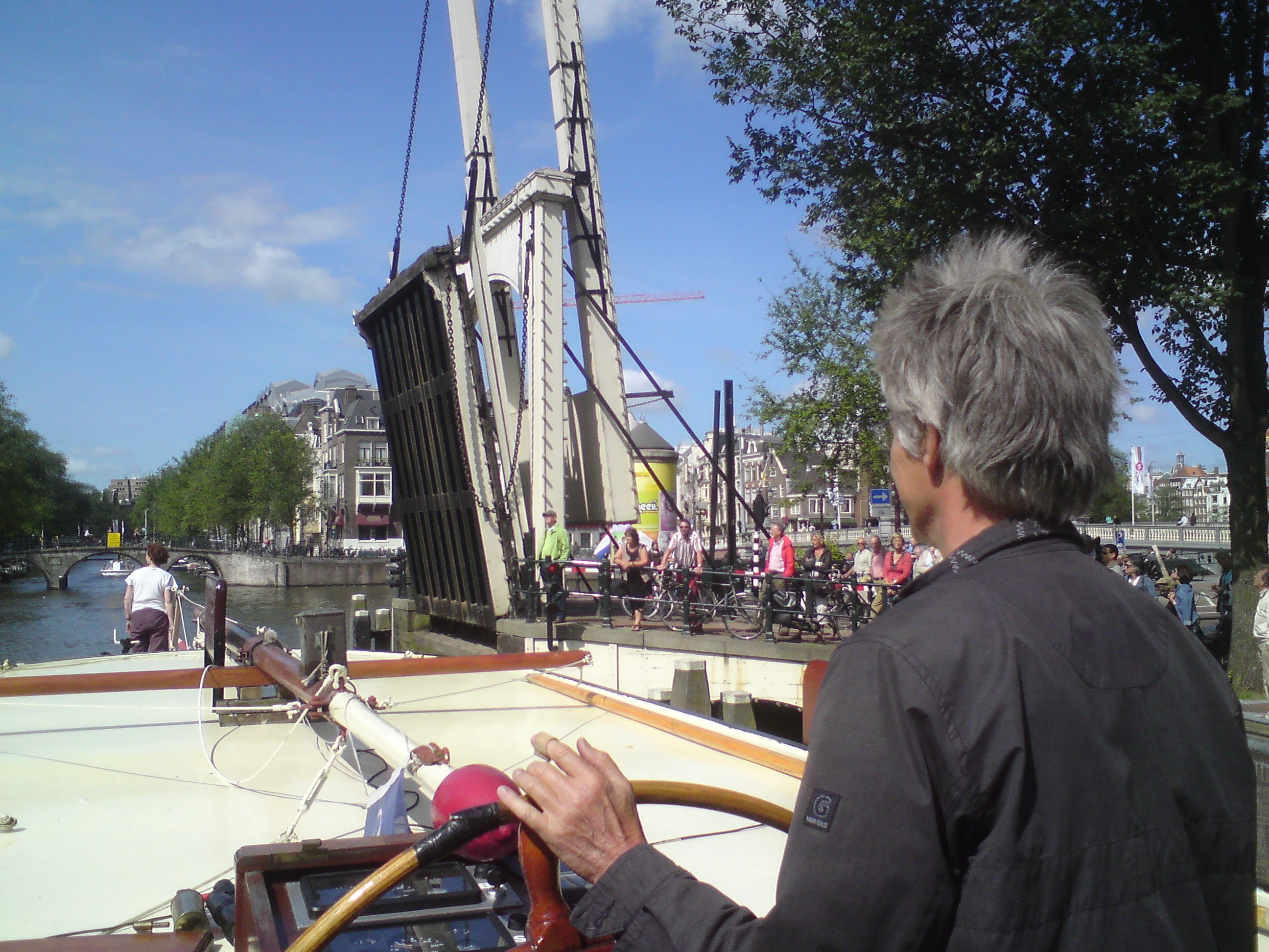 Dick Pels stuurt zijn kruiser door de Nieuwe Herengracht. Voor op het dek zijn vrouw Baukje Prins.   